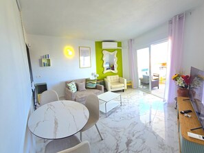 A modern living room with a sofa, armchairs, a coffee table, and a dining table. There is a large mirror on the wall, a TV, and a desk with a computer. The room has a large window with curtains. - Elegant urban retreat in Torremolinos with panoramic terraces (Torremolinos)
