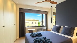 Een moderne hotelkamer met een groot bed, een plafondventilator, een klein rond tafeltje en uitzicht op gebouwen.