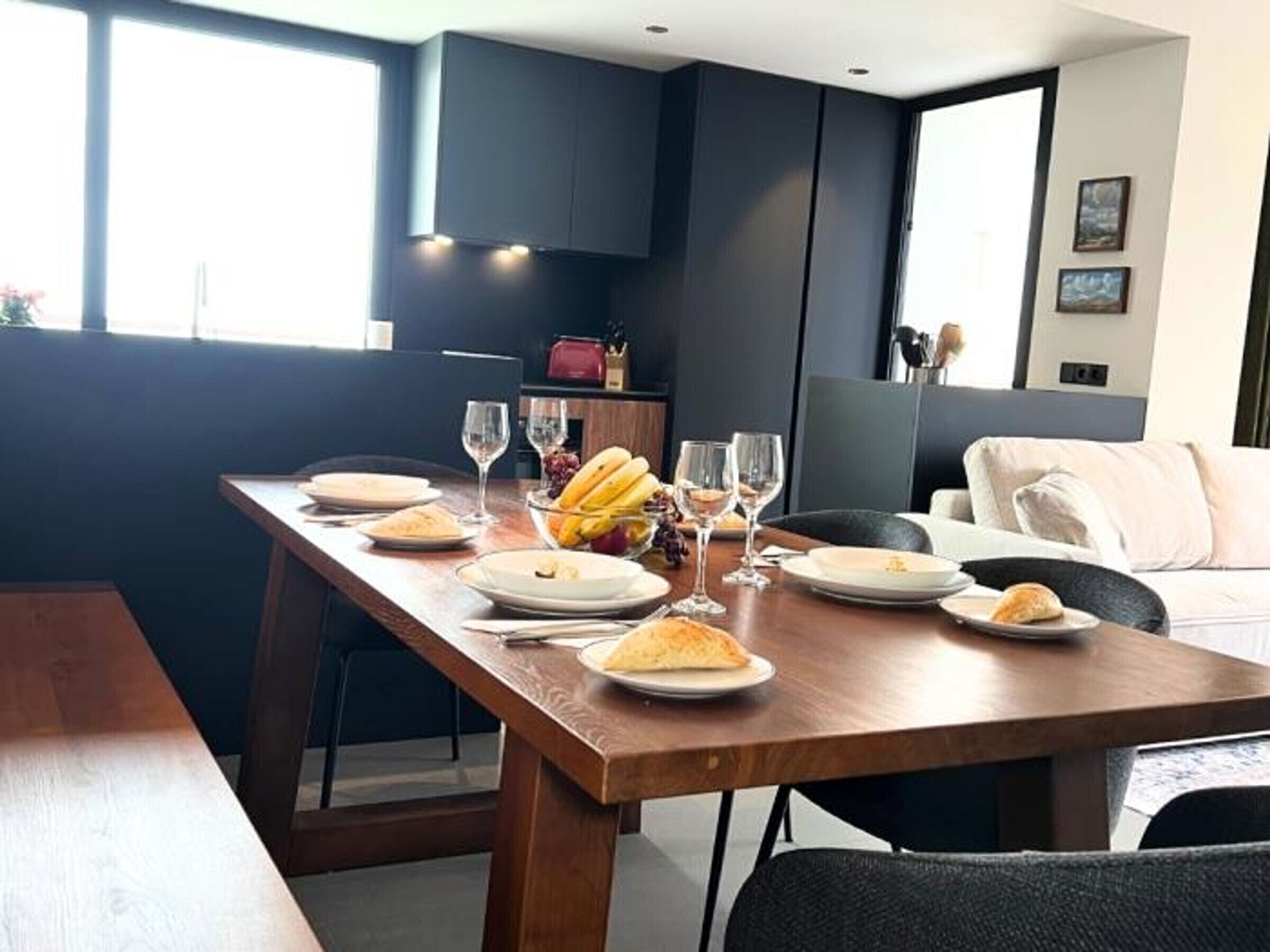 Un comedor con una larga mesa de madera dispuesta para una comida, rodeada de sillas de color oscuro.