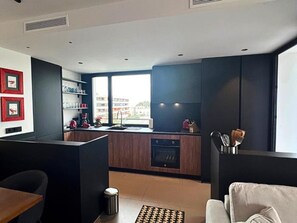 A modern kitchen with dark cabinetry, a built-in oven, and a window providing a view of the city.
