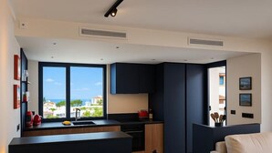 Een moderne keuken met donkere kastjes, een eethoek met een tafel gedekt voor twee, en uitzicht op zee door grote ramen.