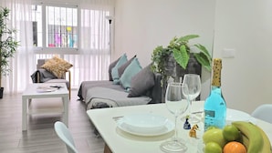 A modern living room with a dining table set for two, a sofa, and a window with sheer curtains. - Elegant 3-Bedroom Apartment in Torremolinos - Wifi and Air Conditioning (Torremolinos)