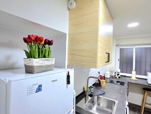 A modern kitchen with a white refrigerator, a sink, and a wooden cabinet above the countertop. - Elegant 3-Bedroom Apartment in Torremolinos - Wifi and Air Conditioning (Torremolinos)