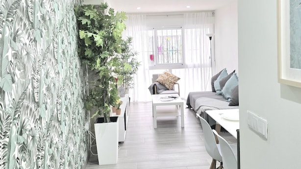 A modern living room with a white sofa, a coffee table, and a large plant. - Elegant 3-Bedroom Apartment in Torremolinos - Wifi and Air Conditioning (Torremolinos)