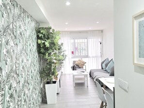 En moderne stue med en hvid sofa, et sofabord og en stor plante.