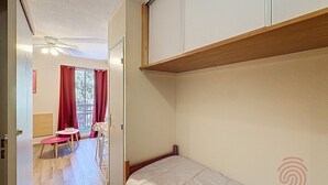 Un dormitorio con una cama litera, una pequeña mesa con sillas y una ventana con cortinas.