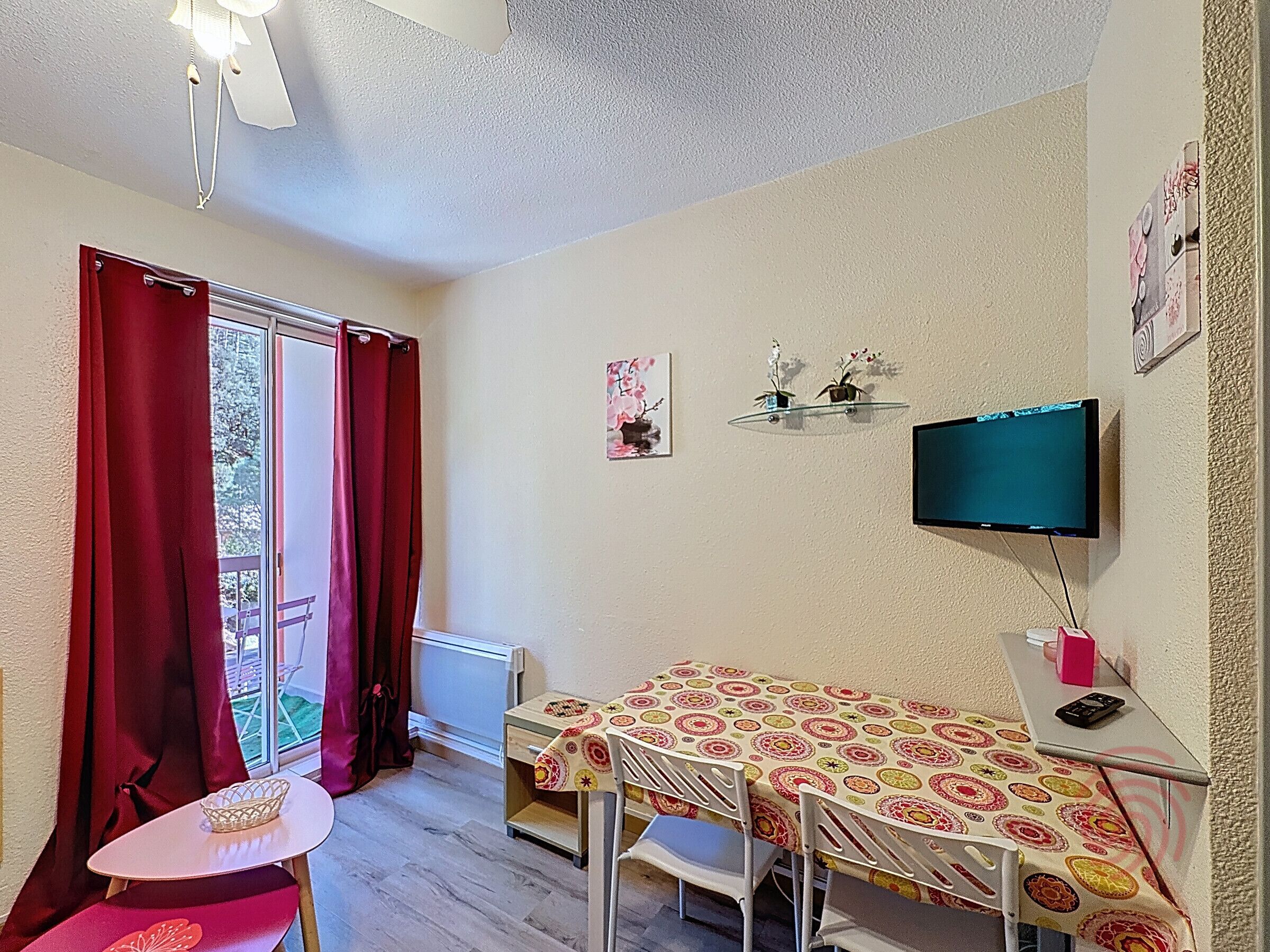 A small room with a bed, a table, a chair, a TV, and a window with curtains.