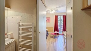 Un pasillo que conduce a una habitación con ventilador de techo, ventana con cortinas rojas y una mesa con sillas.