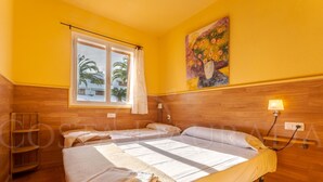 Une chambre avec un lit, une fenêtre avec des rideaux, un tableau au mur et une tête de lit en bois.