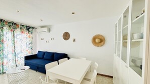Een kamer met een witte tafel en stoelen, een blauwe bank, een gordijn met patroon, en een muur met decoratieve objecten.