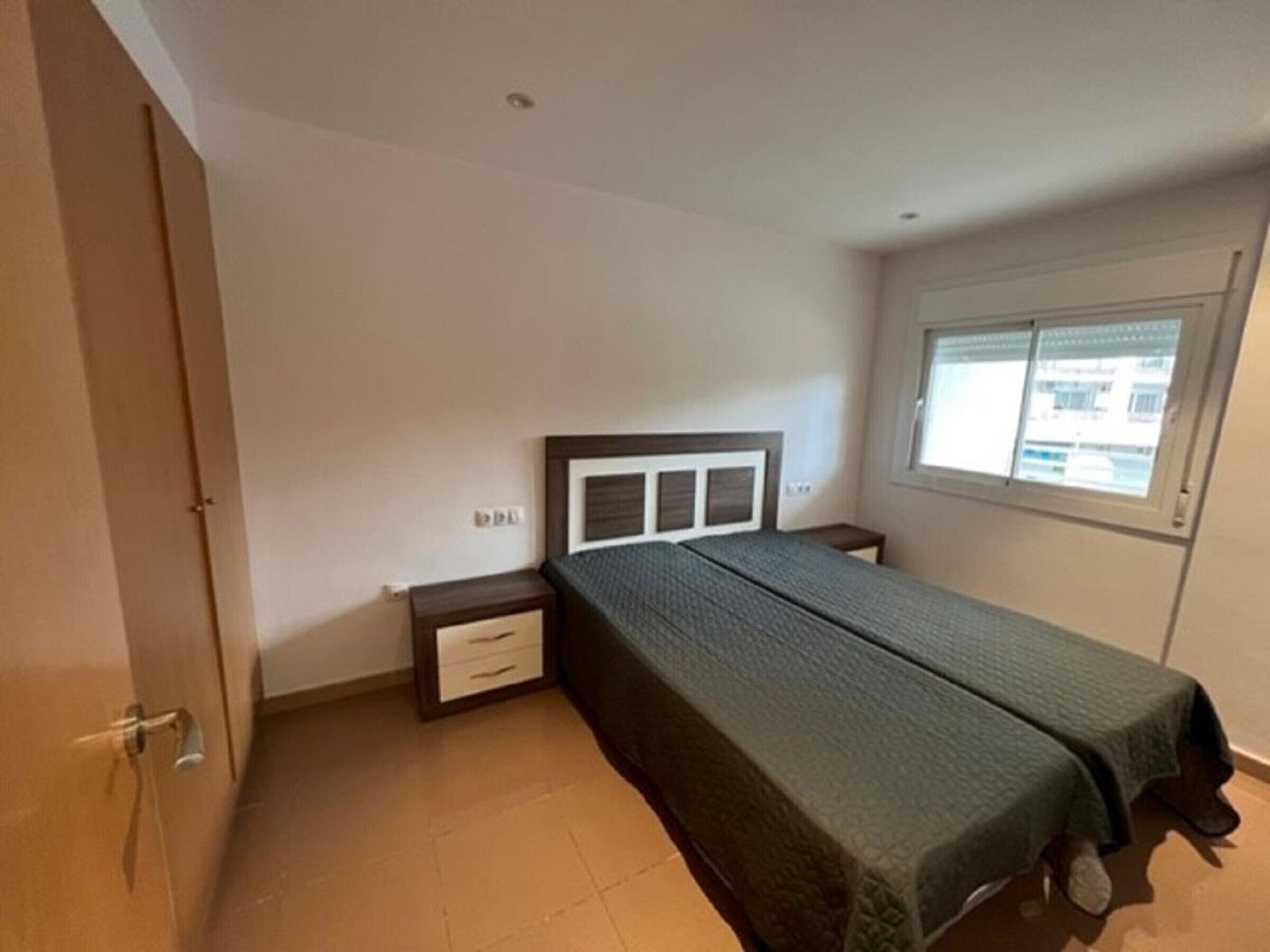Ein Schlafzimmer mit einem Einzelbett, einem Nachttisch, einer Schublade und einem Fenster mit Jalousien.