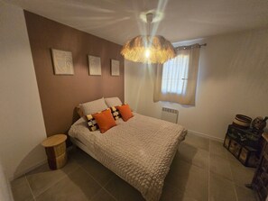 Une chambre à coucher comprenant un lit, une table de chevet, une lampe, une fenêtre avec des rideaux et des œuvres d’art murales.