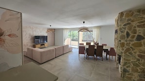 Una sala de estar con sofá, televisor, mesa de comedor, sillas y una pared de piedra.
