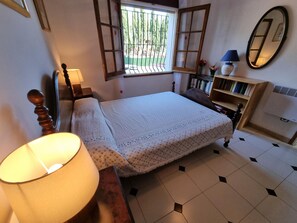 Ein Schlafzimmer mit Bett, Nachttisch, Lampe, Fenster, Bücherregal und Spiegel.