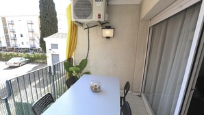 Un balcó amb taula, cadires, un aparell d'aire condicionat i una vista d'un edifici al fons.