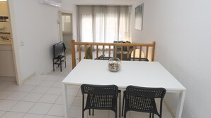 Una zona de menjador amb una taula blanca i quatre cadires negres, una banca de fusta i un vas decoratiu.