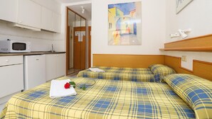 A bedroom with a bed, a bedside table, a microwave, a small fridge, a wardrobe, and a painting on the wall. - Cozy Studio with Terrace, Pools, AC, Near Beach, Sleeps 4 (Salou)