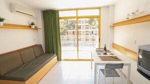 A compact living space with a sofa, a dining table with a chair, a TV, and a balcony with a view of a residential area. - Cozy Studio with Terrace, Pools, AC, Near Beach, Sleeps 4 (Salou)