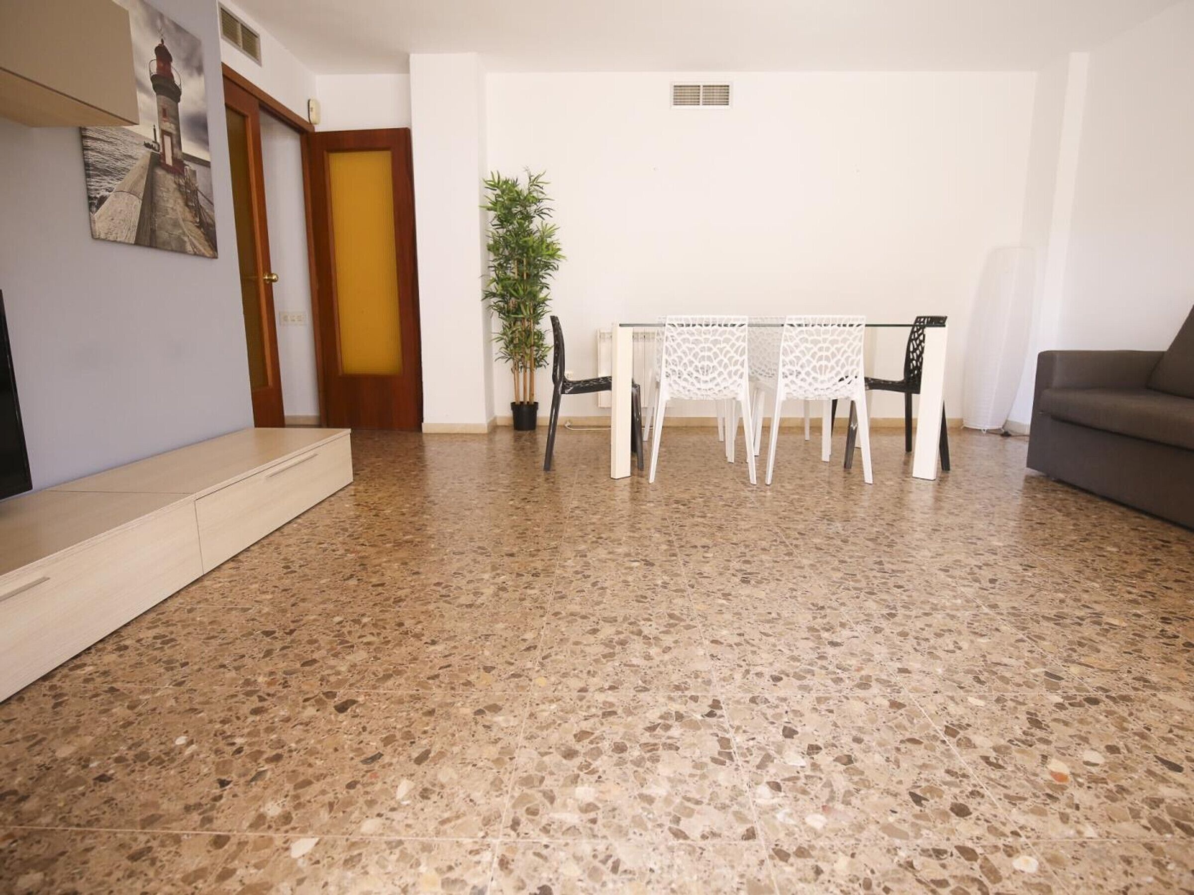 Un saló amb una taula de dinar i cadires, un sofà, una planta en test i un quadre a la paret.