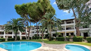 Un hotel con piscina, rodeado de palmeras y un césped cuidado.