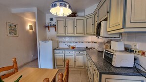 Una cocina compacta con armarios de colores claros, un refrigerador, un microondas, un tostador y un comedor con mesa y sillas de madera.