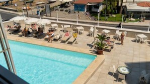 A rooftop pool area with lounge chairs and umbrellas, a small table with a decorative top, and a view of the surrounding area including a building labeled "POTIUM". - Naxos Seaside Escape: Terrace (Giardini Naxos)