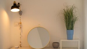 A room with a round mirror, a small table with a blue pot, a wall-mounted lamp, and a power outlet. - Naxos Seaside Escape: Terrace (Giardini Naxos)