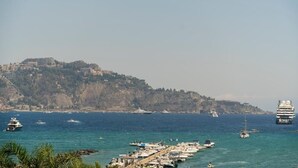 A coastal marina with boats docked, a cruise ship, and a hilly landscape in the background. - Naxos Seaside Escape: Terrace (Giardini Naxos)