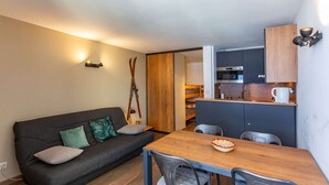En kompakt opholdsstue med sofa, spisebord og tekøkken.