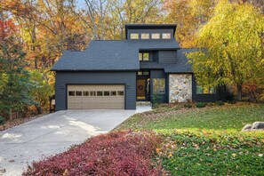 A modern two-story house with a garage, surrounded by autumn foliage.