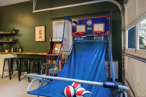 A room with a blue trampoline, two basketball hoops, and a small table with bottles and glasses.