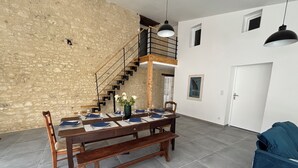 A dining area with a wooden table set for four, a staircase, and a blue sofa in a modern interior.