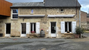 A two-story stone building with a tiled roof, white shutters, and a small balcony.