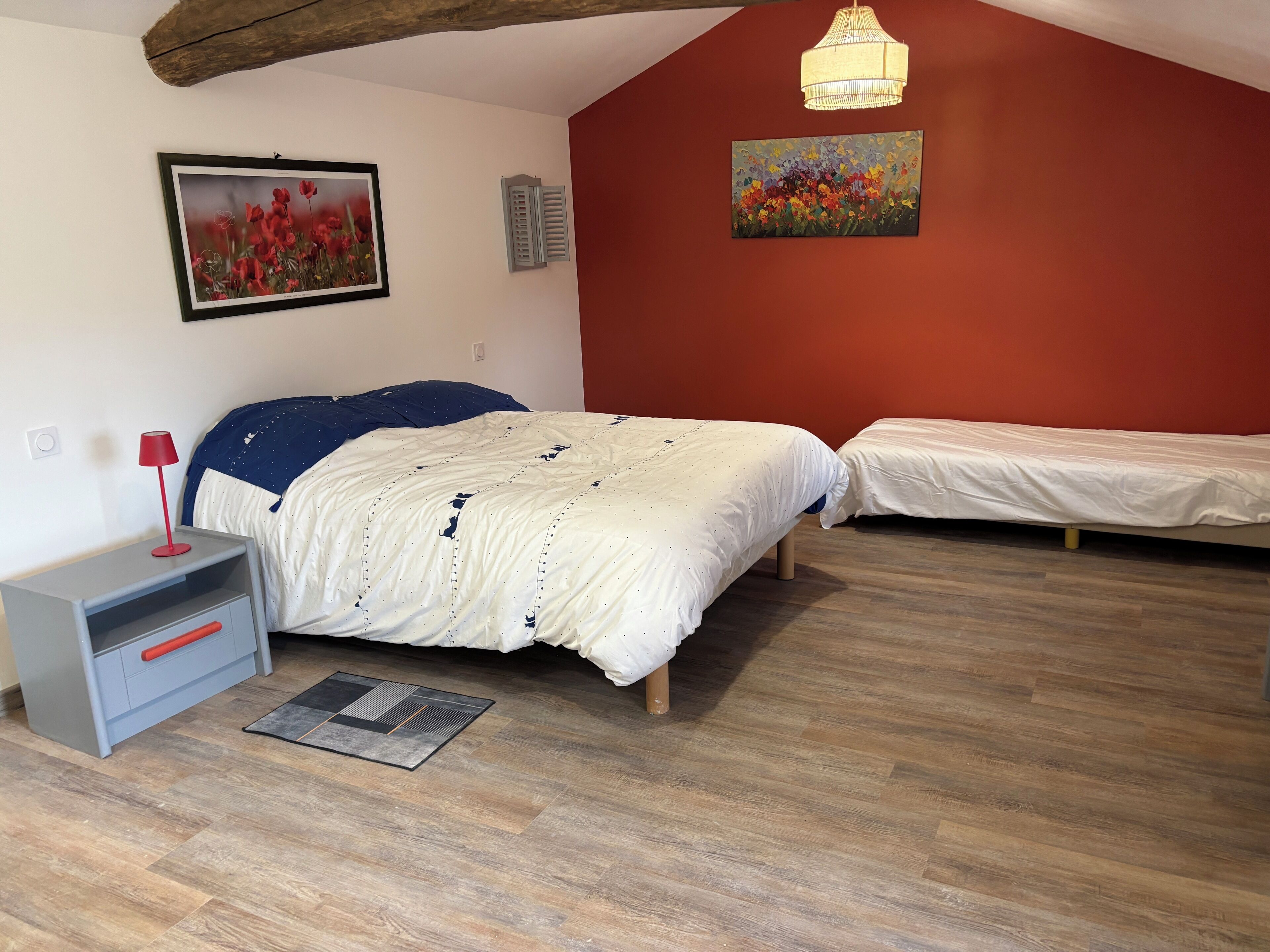 A bedroom with two beds, a nightstand, a lamp, and artwork on the walls.