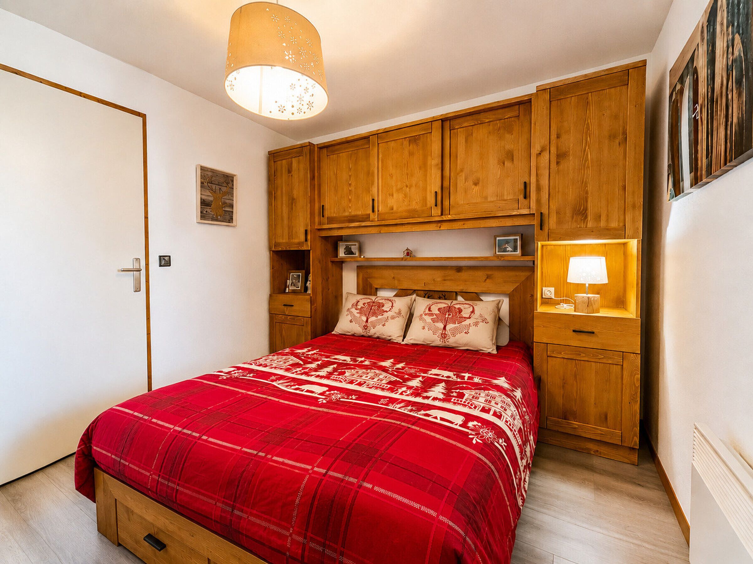 A bedroom with a bed, wooden cabinets, a nightstand, a hanging light fixture, and a door.