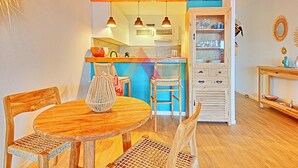 Un coin repas chaleureux avec une table ronde en bois et des chaises en osier, une cuisine dotée de meubles en bois et de luminaires suspendus, ainsi qu’une petite table d’appoint agrémentée d’objets décoratifs.