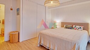 Une chambre à coucher avec un grand lit, un luminaire suspendu, une armoire et une petite poubelle.