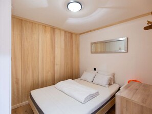 A bedroom with a wooden wardrobe, a bed with white bedding, a bedside table, and a mirror on the wall. - Cozy apartment 4 pers mountain decor near slopes (La Mongie)