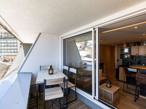 A balcony with a table and chairs, a sliding glass door leading to a kitchen, and a view of buildings outside. - Cozy apartment 4 pers mountain decor near slopes (La Mongie)