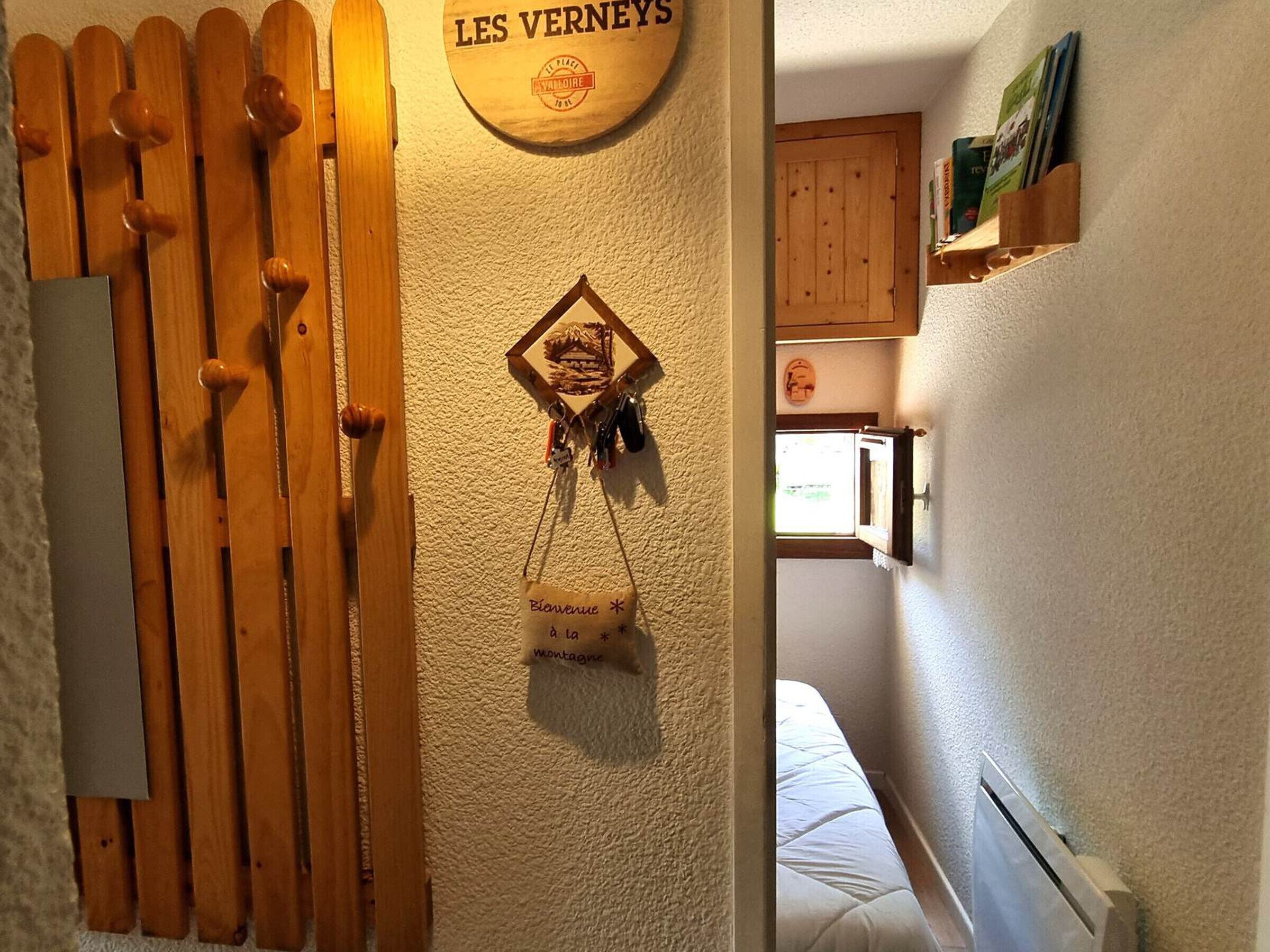 Eine Holztür mit einem Schild darüber, ein an der Wand befestigter Schlüsselhalter und ein Bett im angrenzenden Zimmer.