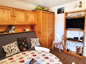 Ein gemütliches Schlafzimmer mit Bett, Holzschrank, Regalen und einem Fernseher.