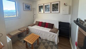 Ein kompakter Wohnbereich mit einer Couch, einem kleinen Holztisch und Blick ins Freie durch ein Fenster.