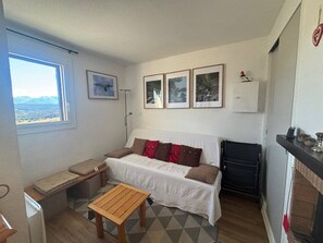 A compact living space with a sofa, a small wooden table, and a view of the outdoors through a window. - 3-Room Apartment in Les Angles with Balcony and Lake View (Les Angles)