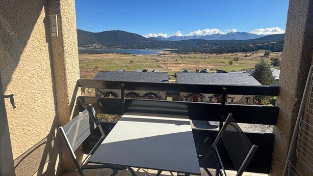 Ein Balkon mit Tisch und Stühlen, der einen malerischen Ausblick auf eine Berg- und Seenlandschaft bietet.