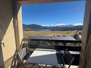 A balcony with a table and chairs, overlooking a scenic landscape with mountains and a lake. - 3-Room Apartment in Les Angles with Balcony and Lake View (Les Angles)