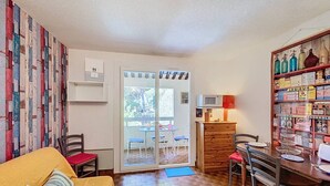 Ett kompakt bostadsutrymme med en soffa, ett matbord, stolar, ett köksområde med mikrovågsugn och en glasdörr som leder ut till ett utomhusområde.
