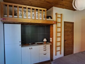 Une petite pièce comprenant un lit superposé, une kitchenette équipée d’une cuisinière et une échelle en bois.
