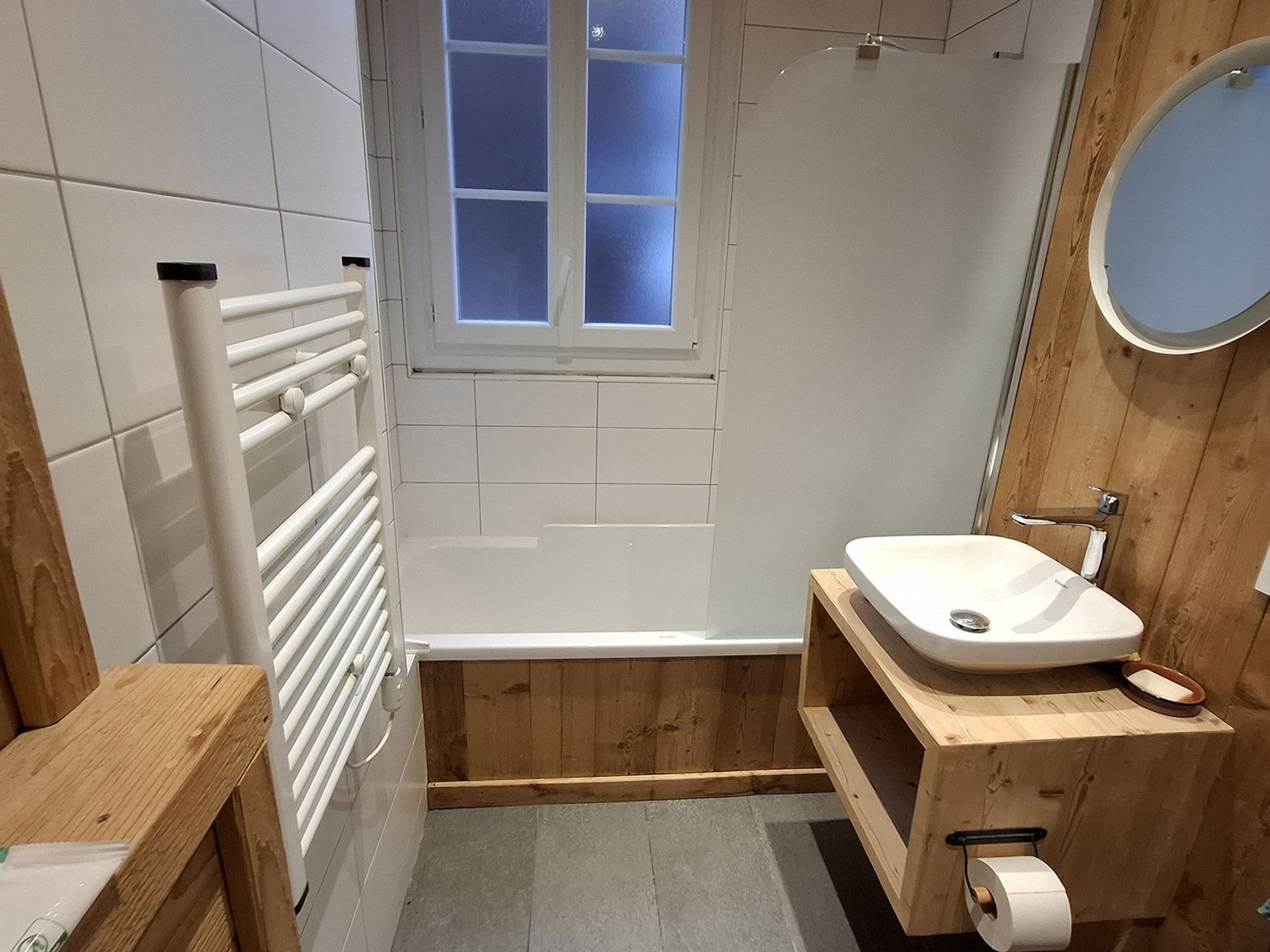 Un baño moderno con una bañera blanca, tocador de madera y una ventana pequeña.