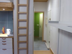 A narrow hallway with a wooden ladder, a kitchenette with a white countertop, and a green door at the end. - Central apartment with large south-facing terrace for 4 people (Arâches-la-Frasse)