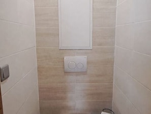 Ein Badezimmer mit weißen Fliesen, einem Wandheizkörper und einer Toilette.
